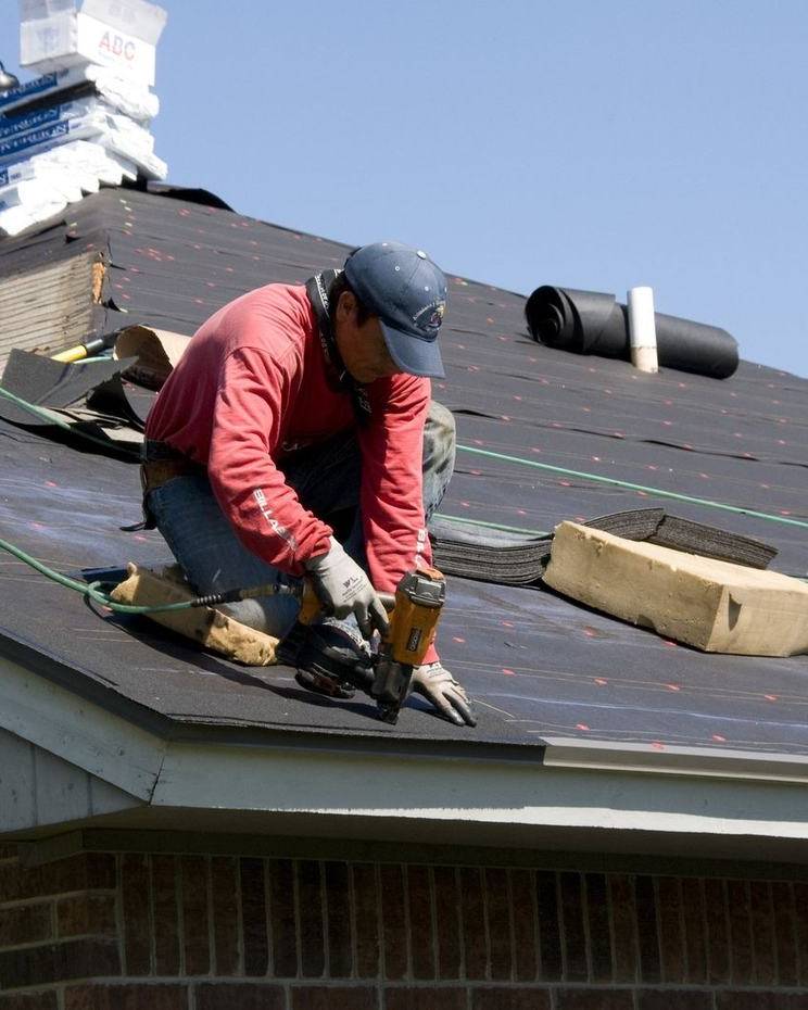 A roofer nails down new shingles